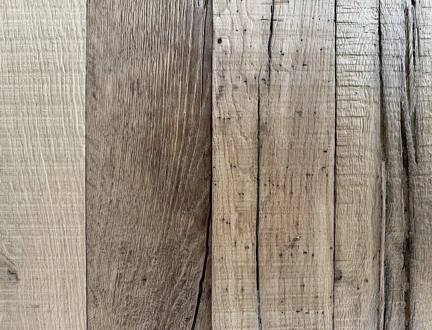 Gros plan d'une surface en bois montrant six planches verticales de bois patiné de différentes nuances avec des motifs et des textures de grain visibles, rappelant le parquet ancien.