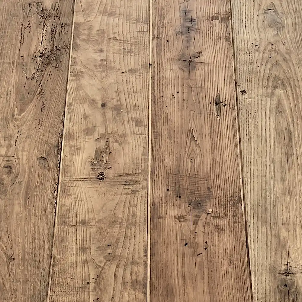  Gros plan de planches de bois présentant des motifs de grain visibles et des imperfections naturelles. Les planches varient en couleur du brun clair au brun foncé, présentant un aspect rustique et usé rappelant un plancher ancien. 
