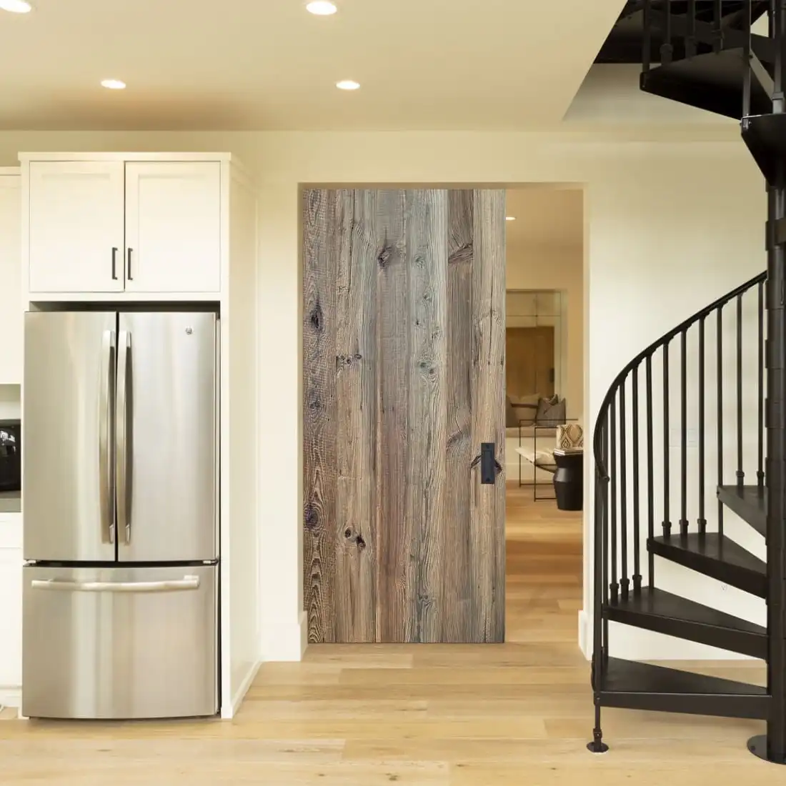  Un intérieur de cuisine moderne avec un réfrigérateur en acier inoxydable à côté d'armoires blanches, une porte de grange coulissante en bois et un escalier en colimaçon noir. 