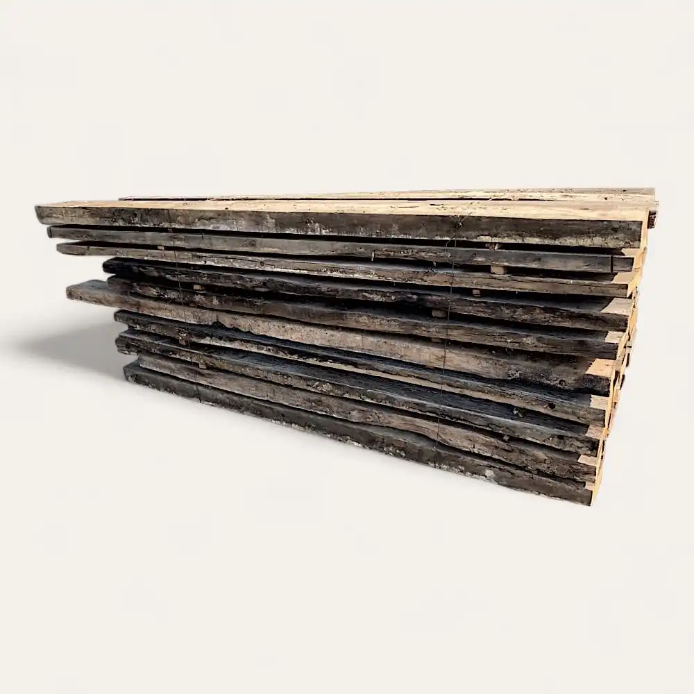  Une pile de madriers anciens de forme irrégulière, fabriqués à partir de vieux chêne, disposés horizontalement pour former une structure triangulaire sur un fond uni. 