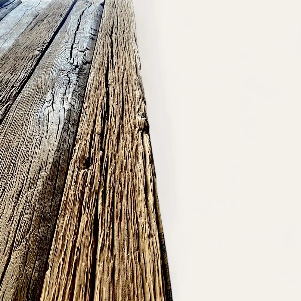  Gros plan de trois planches de bois patinées en vieux chêne sur un fond blanc uni, mettant en valeur les textures rugueuses et l'aspect vieilli des madriers anciens. 
