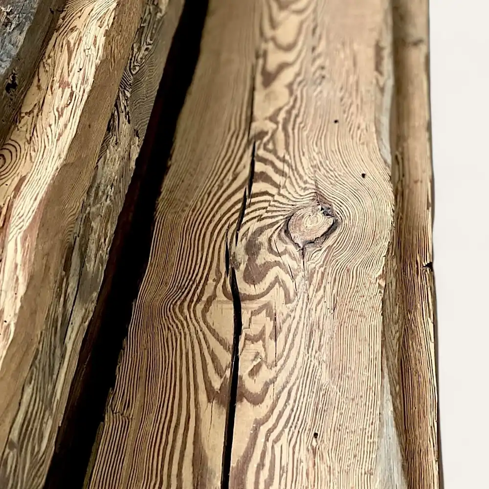  Gros plan de madriers anciens, mettant en valeur des poutres en bois vieillies avec des motifs de grain distincts, des nœuds et des fissures naturelles à la surface du bois. Le bois présente diverses nuances de brun et des variations de texture. 