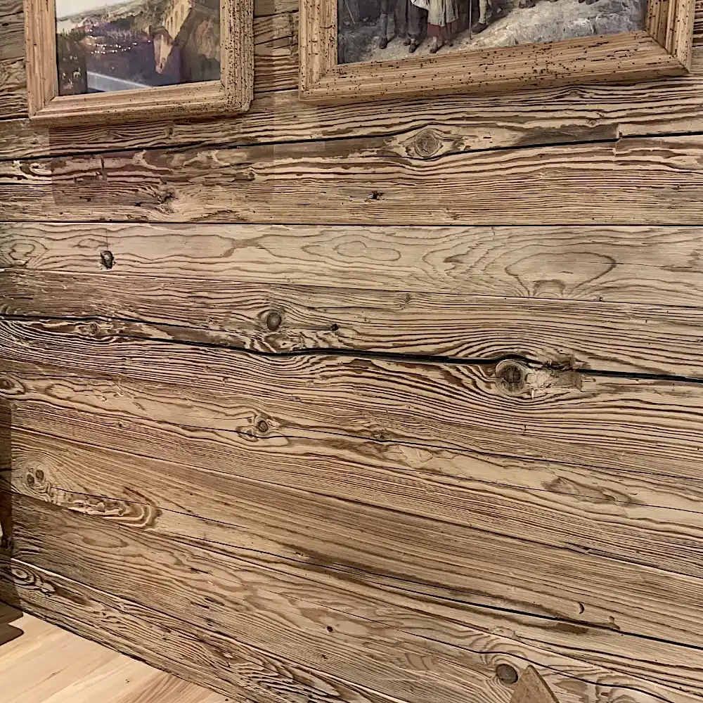  Un mur en bois aux veinures et nœuds apparents, orné de tableaux encadrés, met en valeur le charme des madriers anciens vieux sapin. 