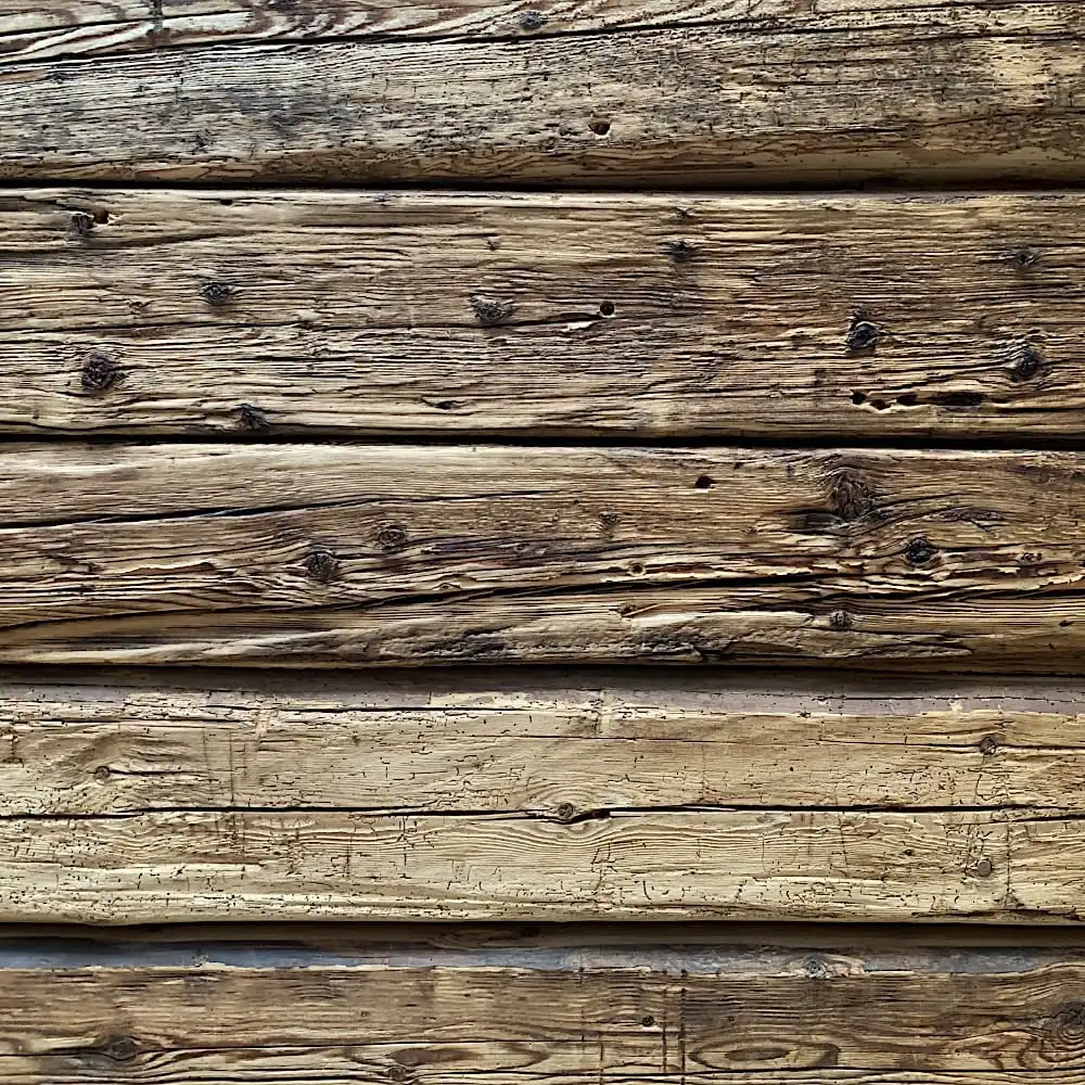  Gros plan d'un mur rustique en bois avec des planches horizontales fabriquées à partir de madriers anciens, mettant en valeur des motifs de grain distinctifs, des nœuds et les textures altérées du vieux sapin. 