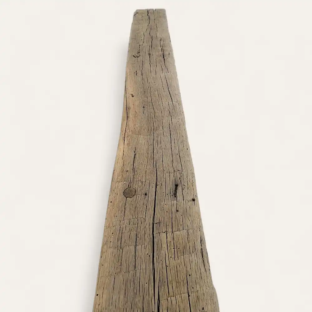  Une longue planche de bois patinée avec des fissures et des nœuds visibles, ressemblant à des poutres anciennes de récupération, sur un fond blanc uni. 