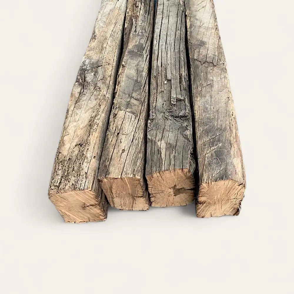  Quatre morceaux de poutres en bois patiné, ressemblant à des poutres anciennes de récupération, sont disposés côte à côte sur une surface claire. 