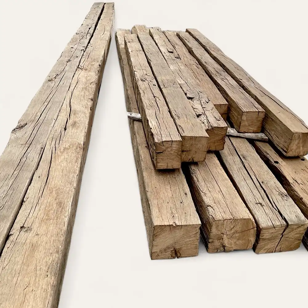  Une pile de poutres en bois patinées de différentes tailles (poutres anciennes de récupération) repose sur un fond clair. 