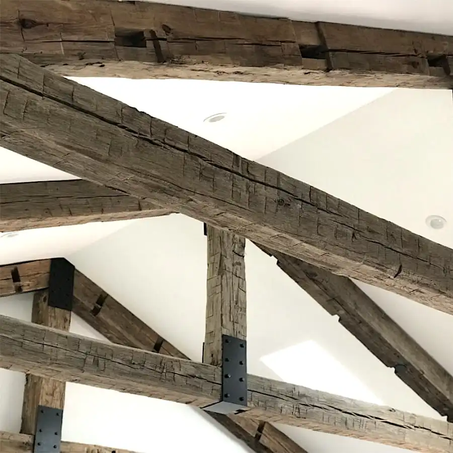  Poutres apparentes en bois avec supports métalliques sur un plafond blanc, comportant des poutres anciennes de récupération. 