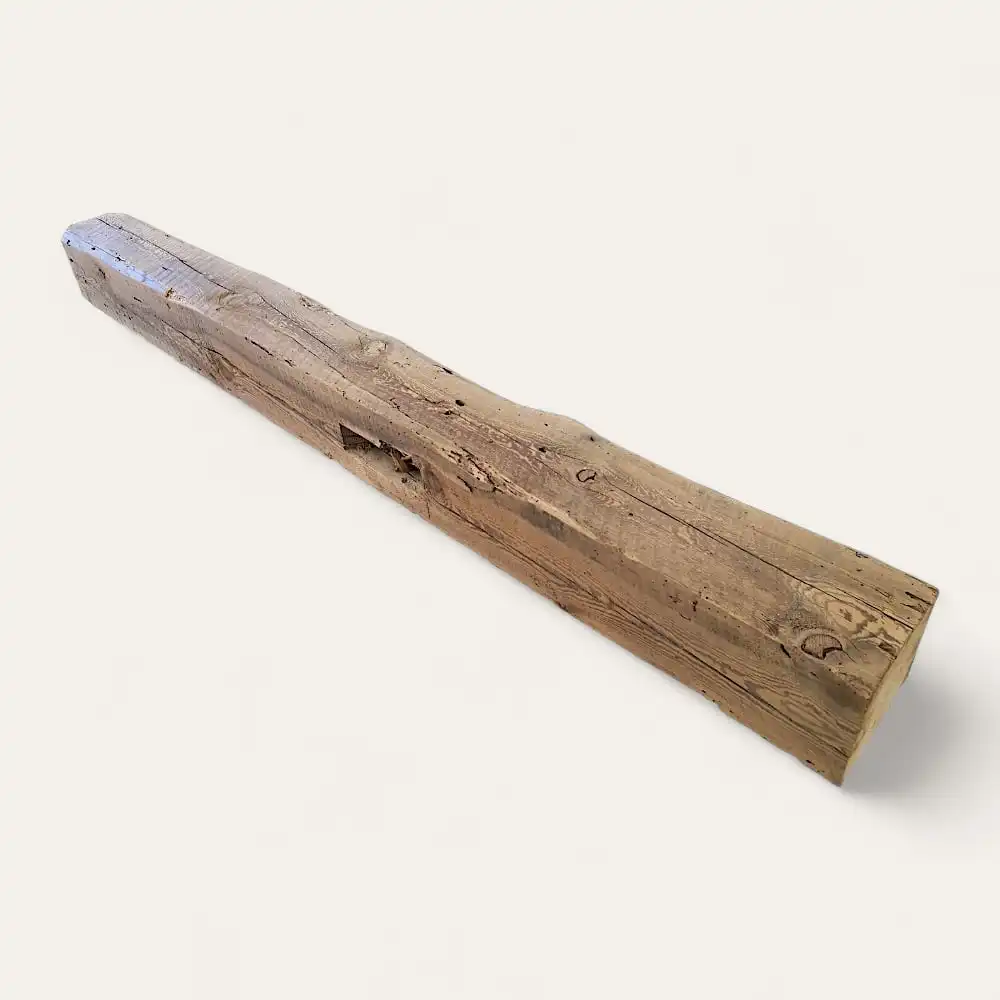  Une poutre en bois patiné à la texture naturelle et rugueuse et aux nœuds apparents, rappelant les poutres anciennes de récupération, posée sur un fond uni blanc. 