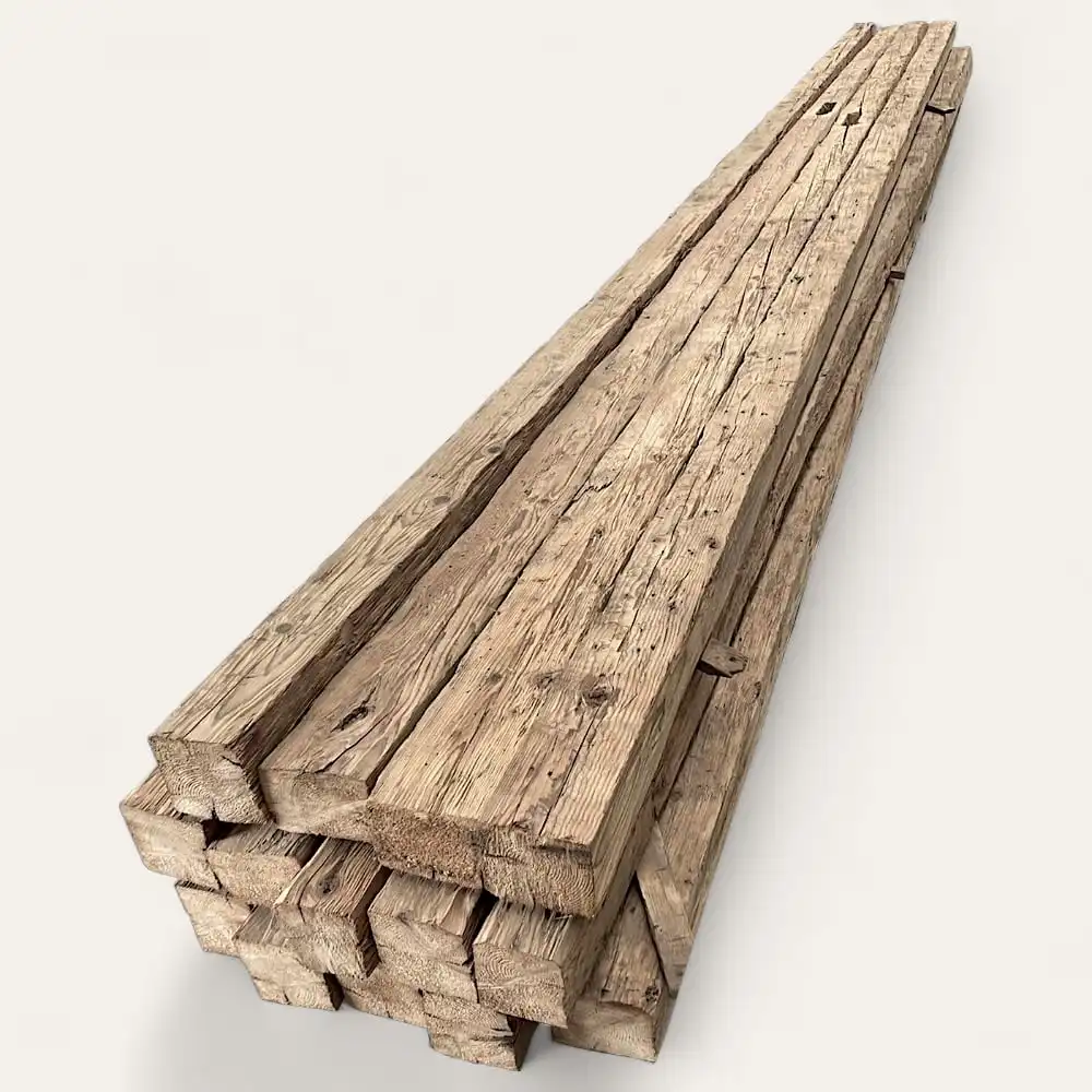  Une pile de planches de bois patinées, ou poutres anciennes de récupération, soigneusement disposées, affichant un grain et une texture visibles, sur un fond uni. 