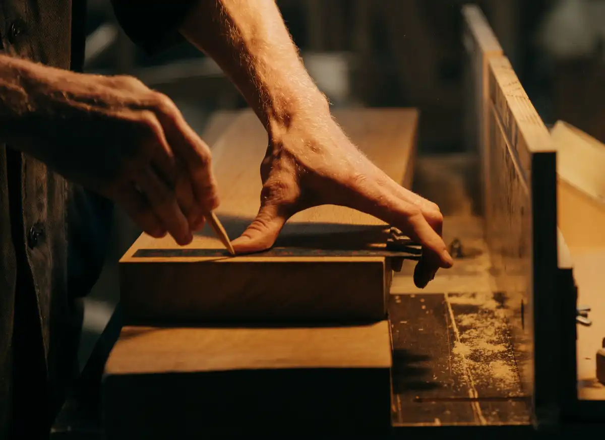 Travail manuel du bois, mains mesurant une planche avec un crayon.