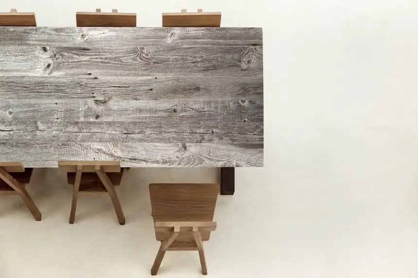 Table avec un plateau en bois gris aux textures rustiques, accompagnée de chaises en bois marron clair, sur un fond clair et uniforme.
