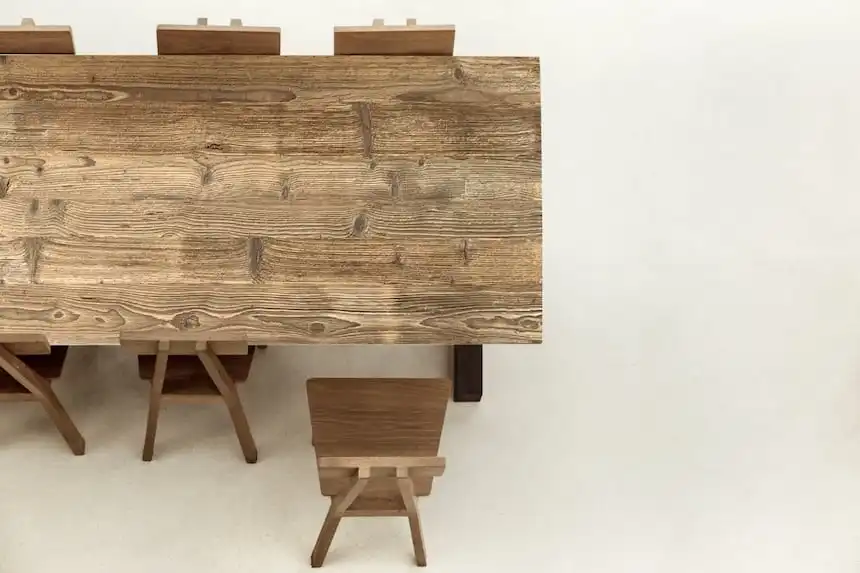 Table à l'ancienne avec un plateau en bois aux motifs de grain prononcés et une finition brune, entourée de chaises assorties, sur un fond neutre.