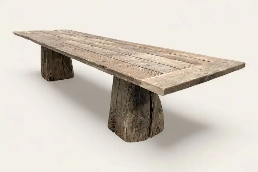 Table de salle à manger rustique avec des pieds massifs ressemblant à des troncs d'arbres, en bois avec une finition vieillie, sur fond blanc.