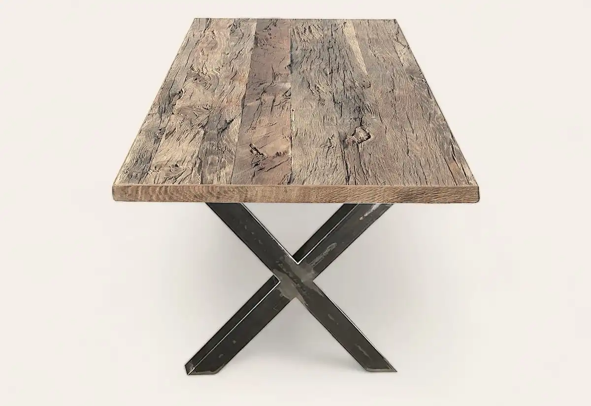 Table carrée rustique avec plateau en bois brut et base croisée en métal noir, mélangeant textures naturelles et design industriel.