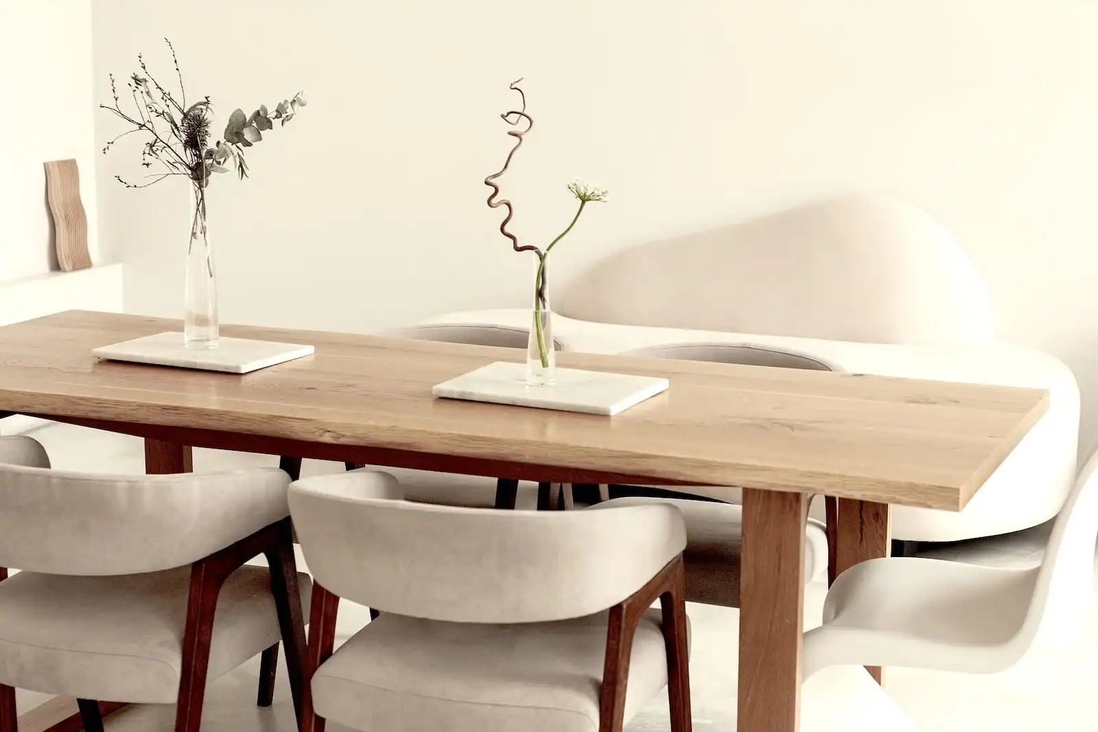 Intérieur chic avec table en bois ancien, chaises modernes en tissu gris, vases minimalistes sur la table, dans une salle à manger épurée et lumineuse.