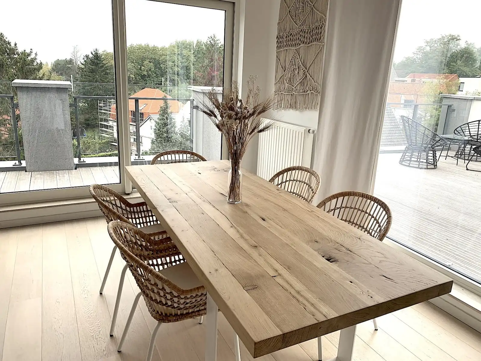  Espace repas élégant avec table en bois rustique et chaises en rotin, grande fenêtre donnant sur un balcon et décoration murale bohème. 