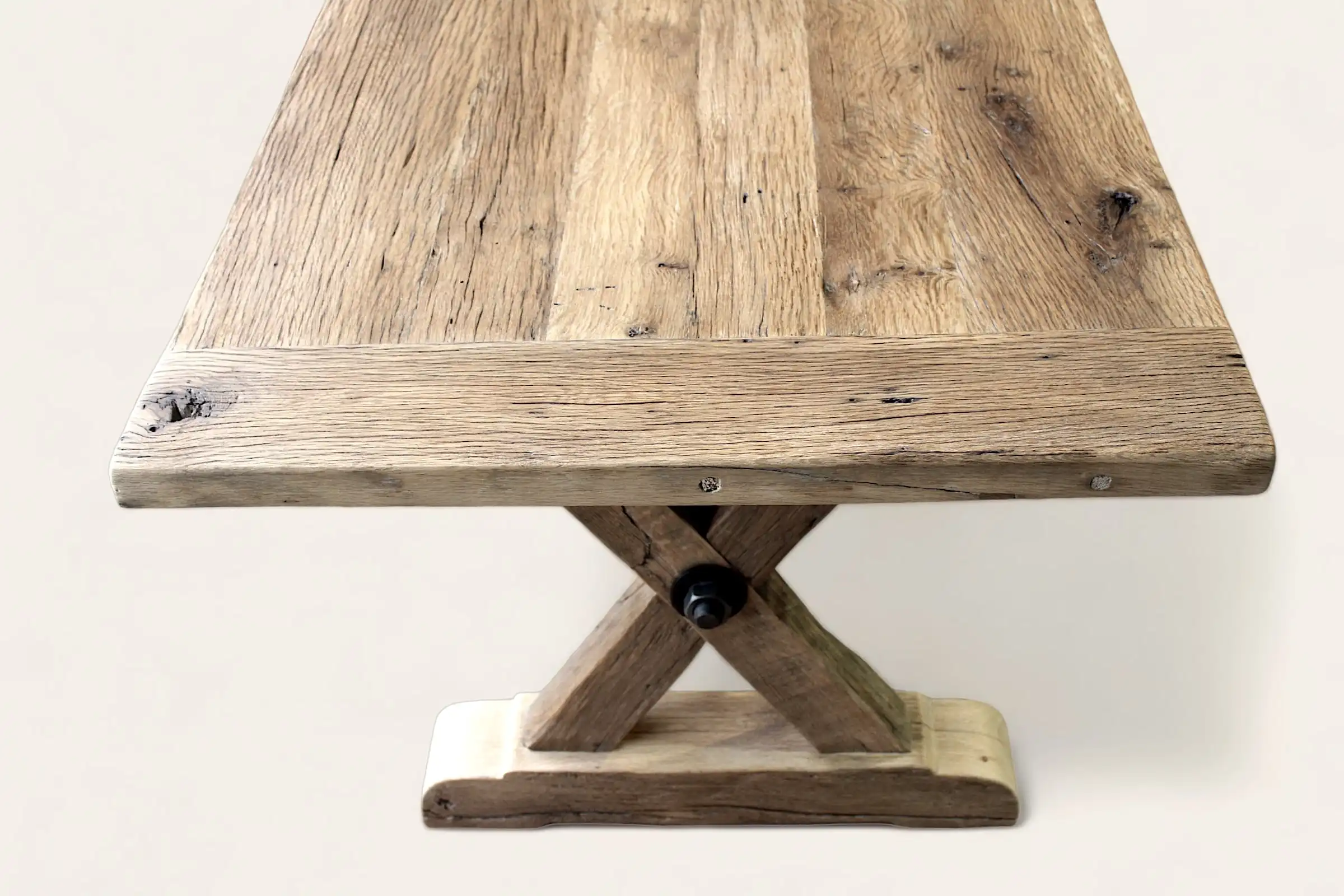  Détail du coin d'une table rustique en bois ancien avec des nœuds et des marques naturelles, reposant sur une base en X robuste, mettant en avant la fusion du charme rustique et de la solidité. 