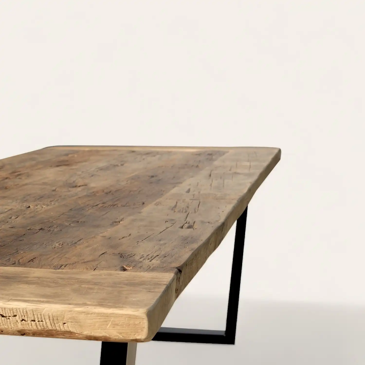  Gros plan sur le coin d'une table rustique en bois ancien, mettant en évidence la texture riche et les veines naturelles du bois sur un support en métal noir, parfaite pour un intérieur élégant et naturel. 