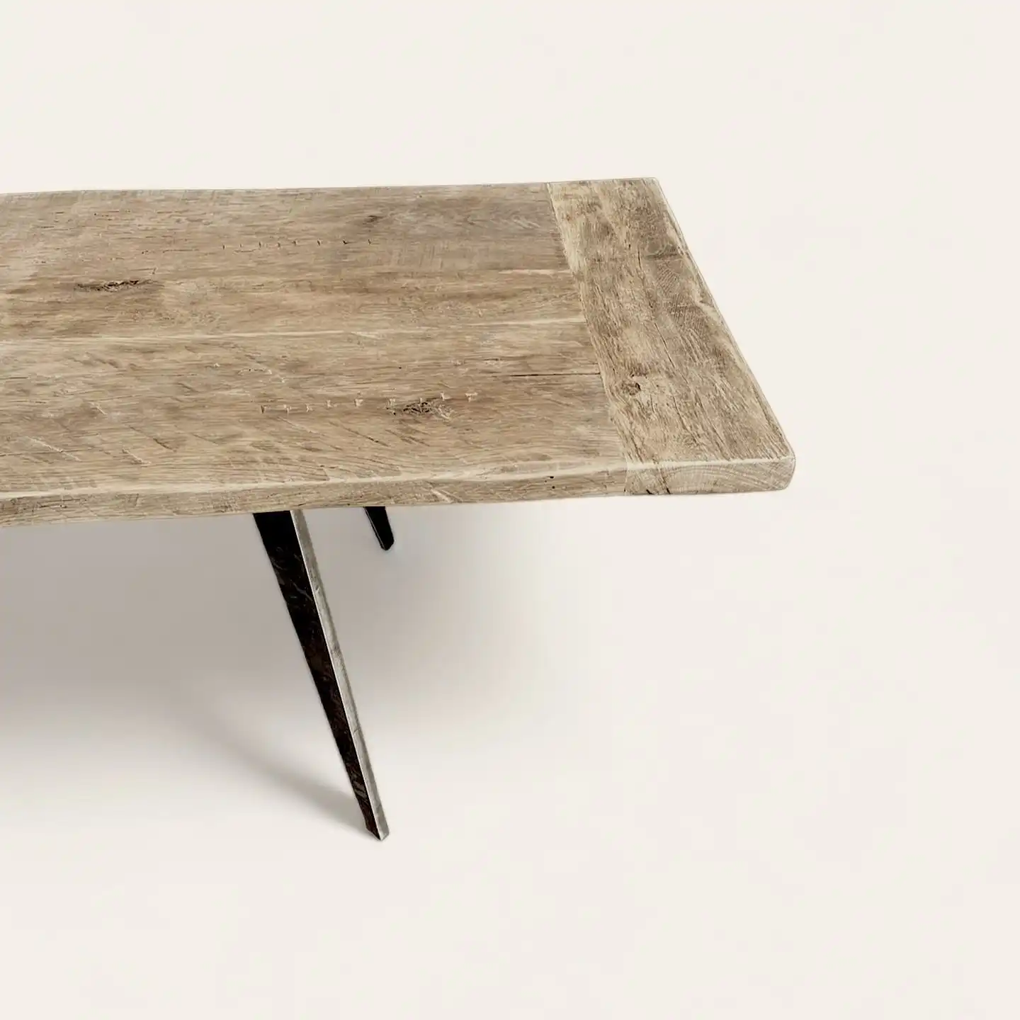  Vue en angle de la texture détaillée d'une table rustique en bois ancien avec une finition naturelle et des pieds en métal inclinés, parfaite pour un design intérieur qui valorise les matériaux durables et l'artisanat. 