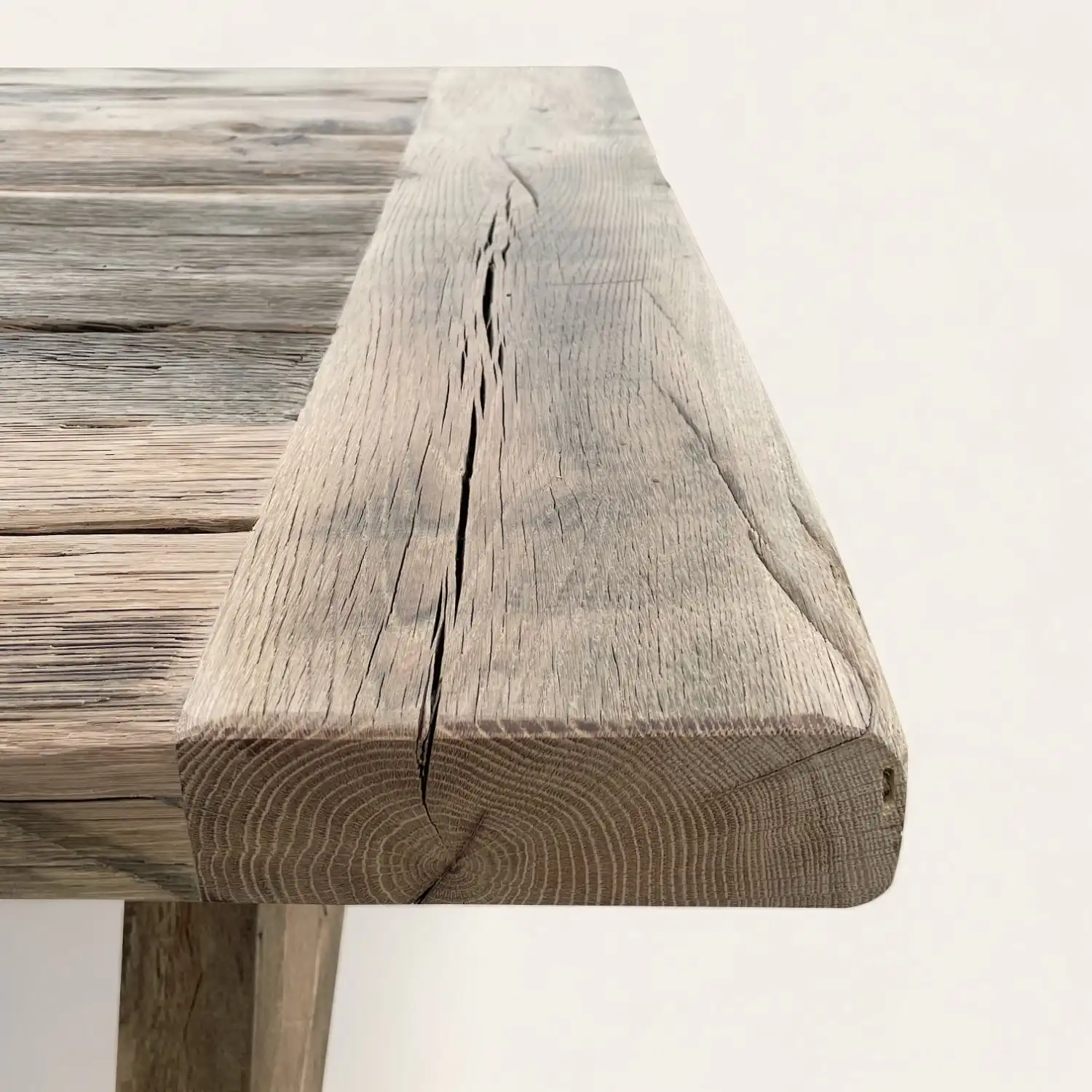  Détail de l'angle d'une table de style fermette, mettant en valeur le bois ancien avec des fissures et des motifs de croissance annuels distincts, évoquant l'histoire et la robustesse naturelle du matériau. 