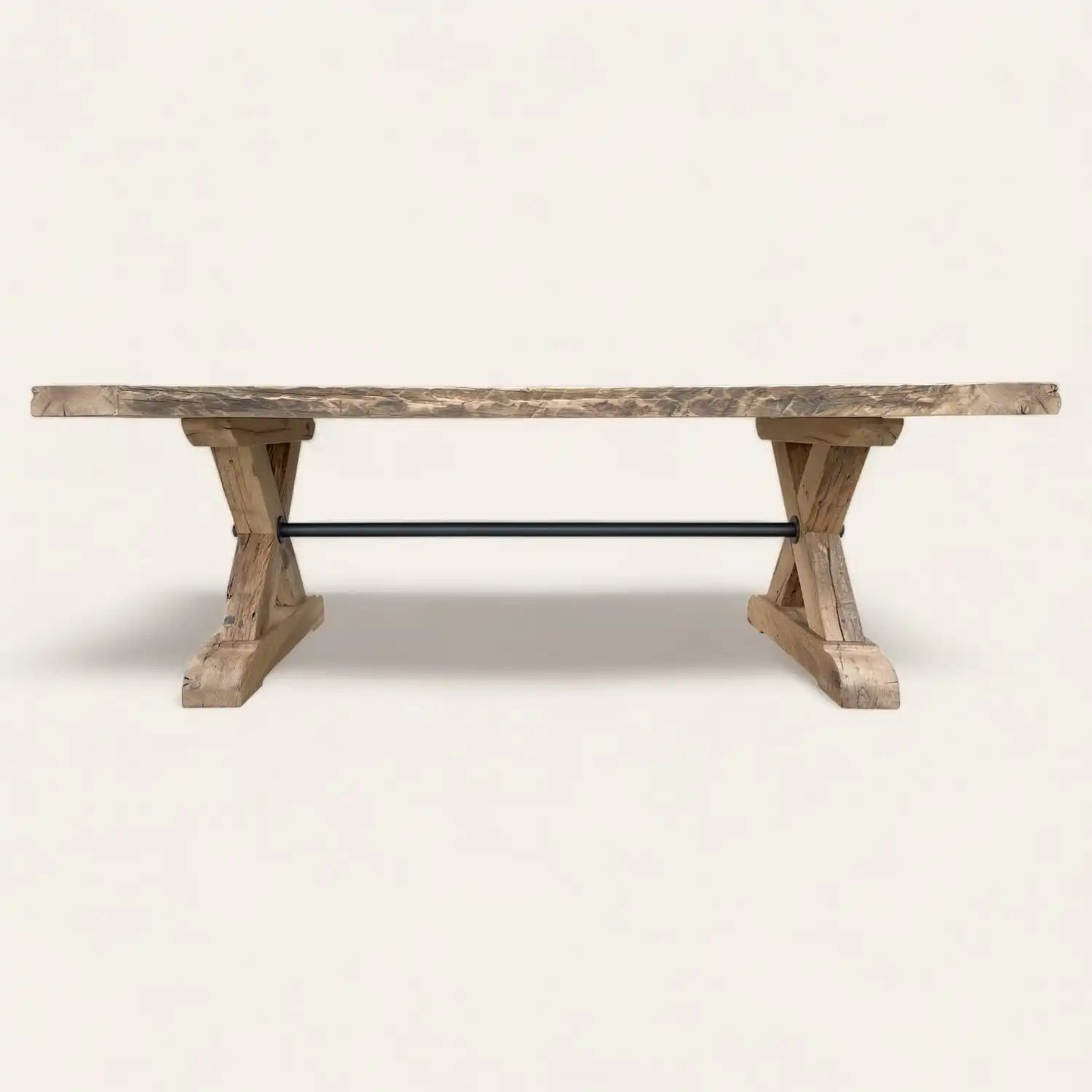  Vue latérale d'une longue table de ferme rustique avec des pieds en X caractéristiques et une barre de soutien métallique horizontale, illustrant un mélange d'artisanat traditionnel et de design industriel moderne. 