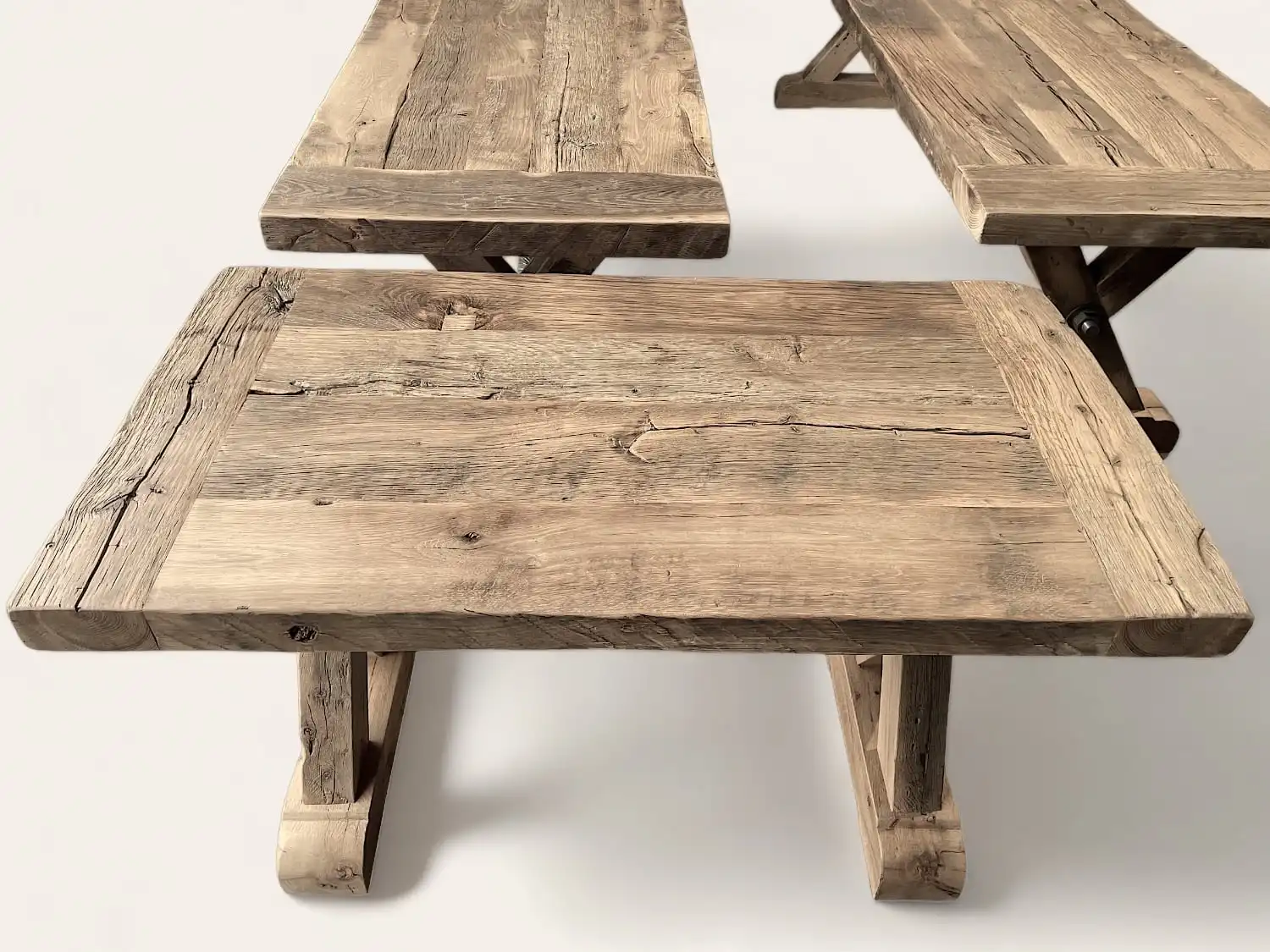 Tables robustes en bois ancien, avec une finition texturée mettant en valeur les noeuds et les fissures naturelles du bois, incarnant l'esprit rustique d'une fermette.