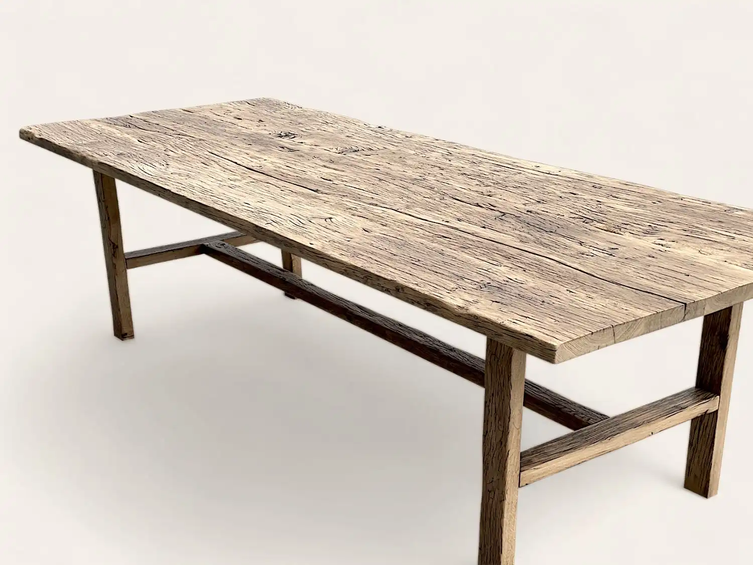 Une longue table rustique en bois Chene massif avec une surface rugueuse et texturée et des pieds robustes sur un fond uni.