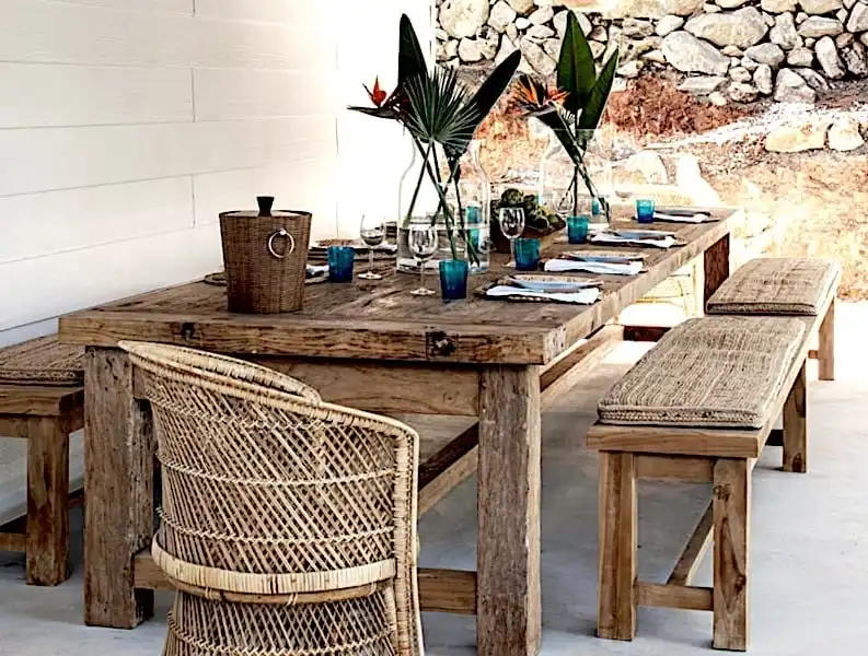 Une table à manger rustique avec des chaises en osier et un mur en pierre.