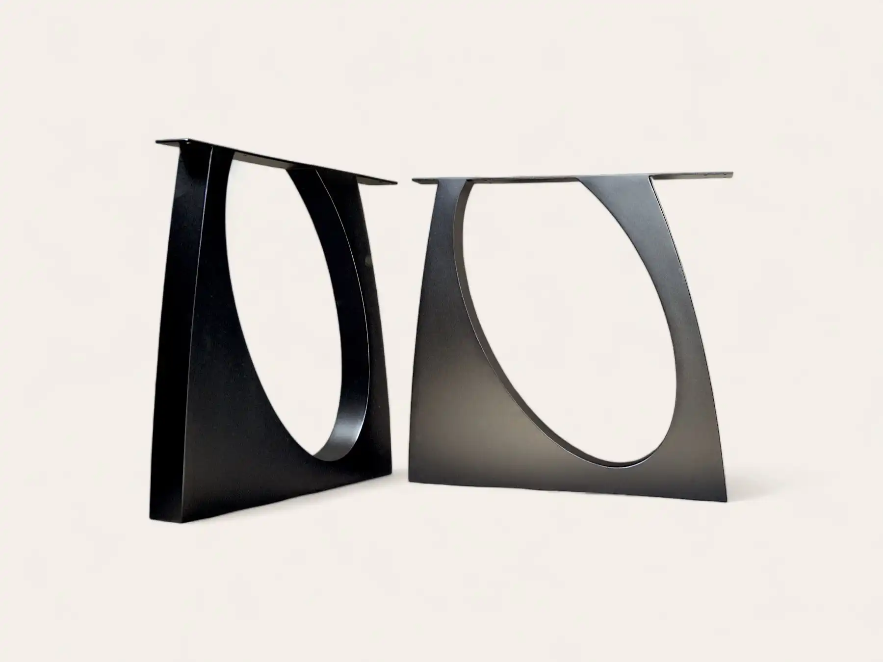 Deux pieds de table en metal noirs modernes avec un motif découpé abstrait sur fond beige.