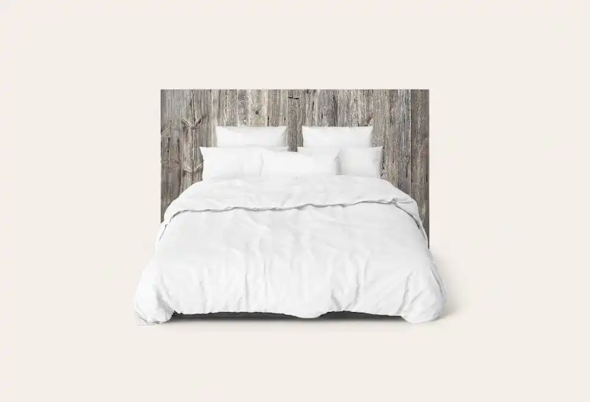Un lit soigneusement fait avec une literie blanche sur une tête de lit en bois rustique et un fond uni.