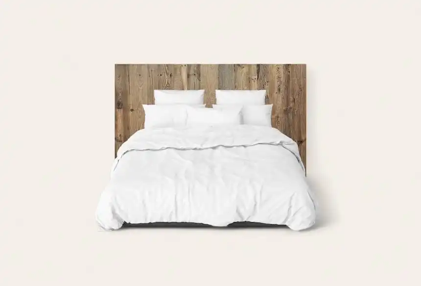 Un lit bien fait avec une literie blanche et une tête de lit en bois ancien contre un mur uni.