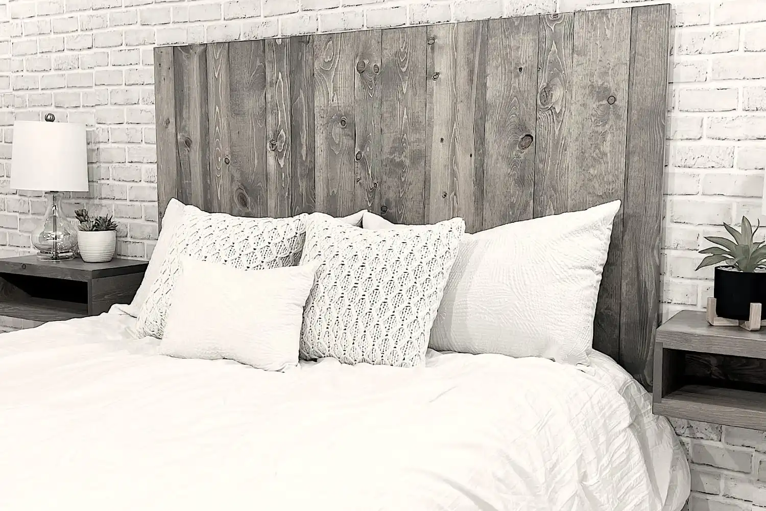 Image monochrome d'un lit soigneusement fait avec une tête de lit en bois rustique, une literie blanche et des oreillers assortis.